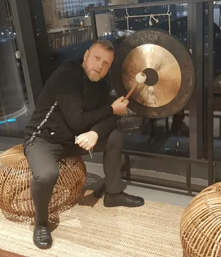 Sitting beside the office gong with the mallet against it, city out the window.