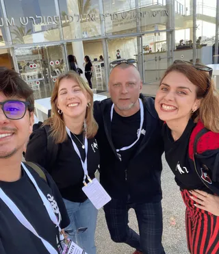 Four of us outside a conference hall, arms round each other, badges on.